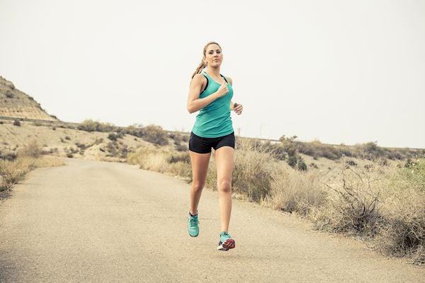 sport woman running on asphalt dirty road with dry desert landscape background training hard